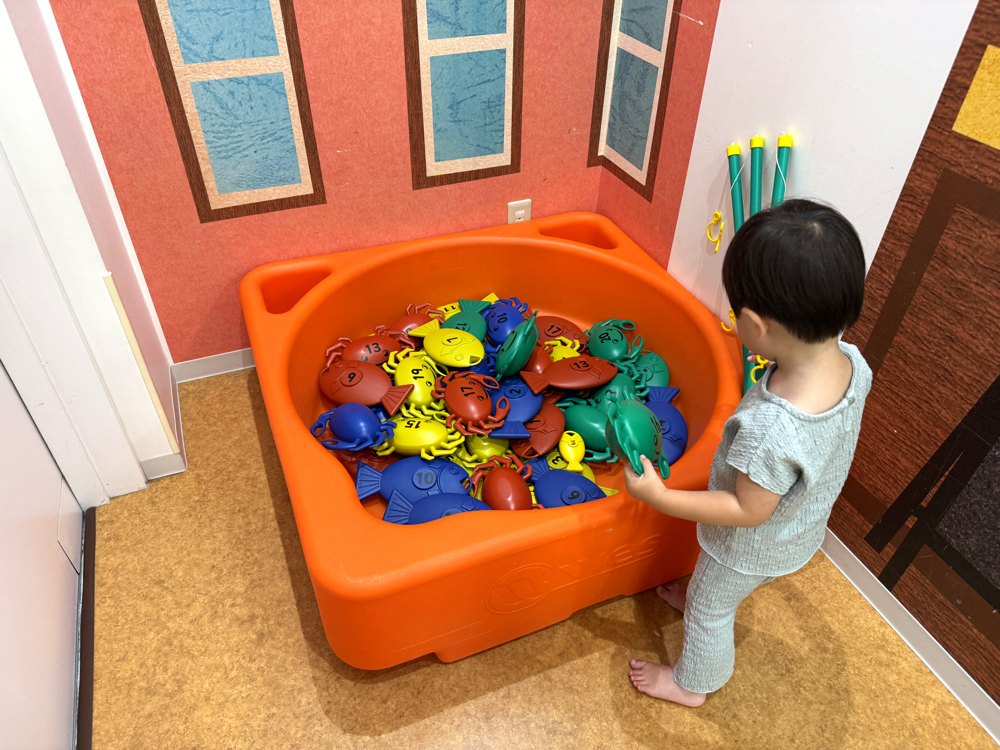 オレンジ色のいけすに魚やカニのおもちゃが入った、つり遊びのコーナー